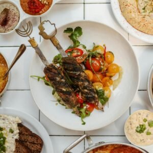 Delicious Middle Eastern spread featuring kebabs, dips, hummus, and traditional breads on a white ceramic background.